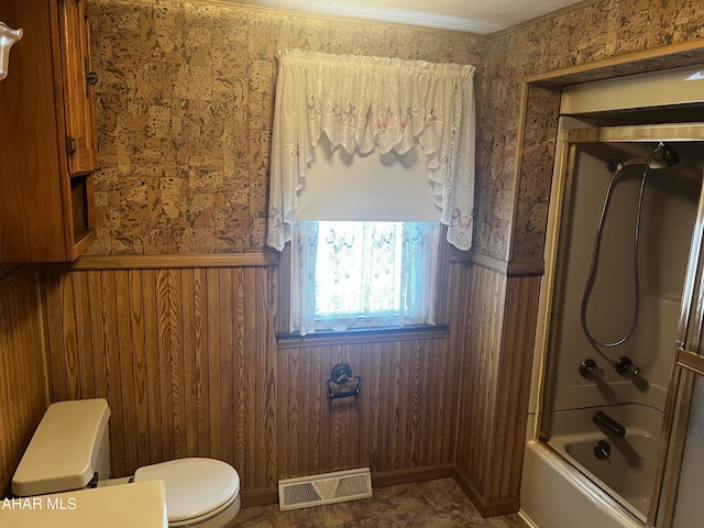 full bathroom featuring toilet, wooden walls, shower / bath combination with glass door, visible vents, and wainscoting