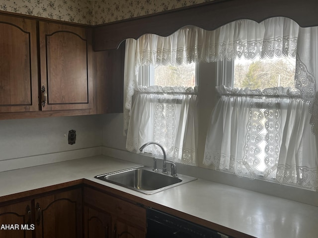 kitchen with black dishwasher, light countertops, a sink, and wallpapered walls