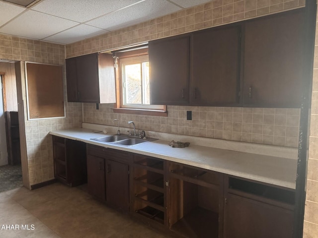 kitchen with sink, a paneled ceiling, dark brown cabinets, and light tile patterned flooring