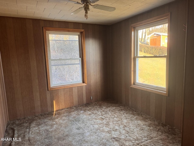 empty room with ceiling fan, a wealth of natural light, wood walls, and carpet