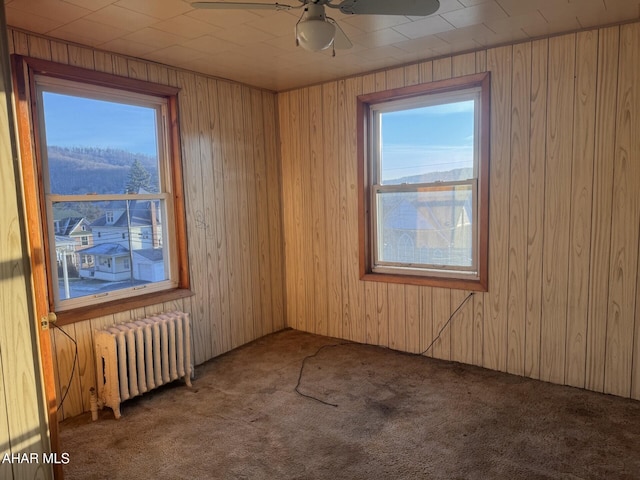 spare room with carpet, radiator, ceiling fan, wooden walls, and a mountain view