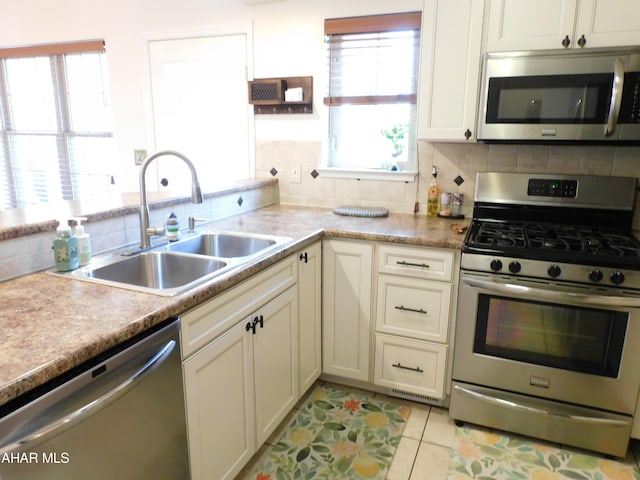 kitchen featuring sink, stainless steel appliances, light tile patterned flooring, decorative backsplash, and white cabinets