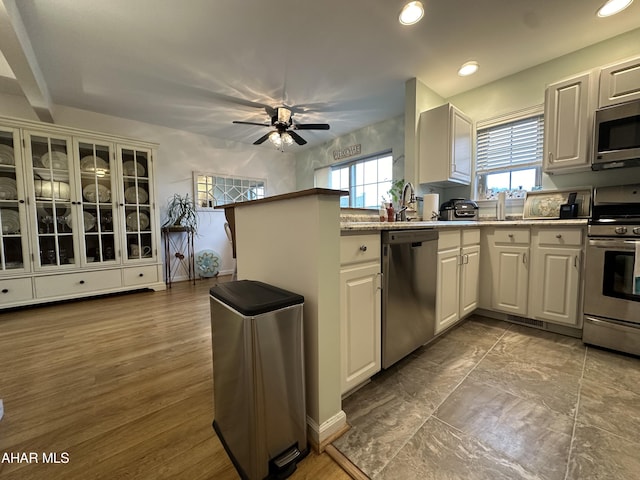 kitchen featuring kitchen peninsula, stainless steel appliances, ceiling fan, wood-type flooring, and white cabinetry