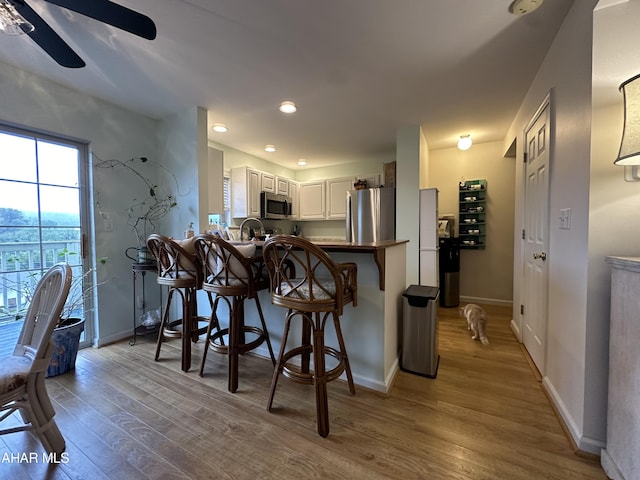 kitchen with a breakfast bar, light hardwood / wood-style floors, white cabinetry, and appliances with stainless steel finishes