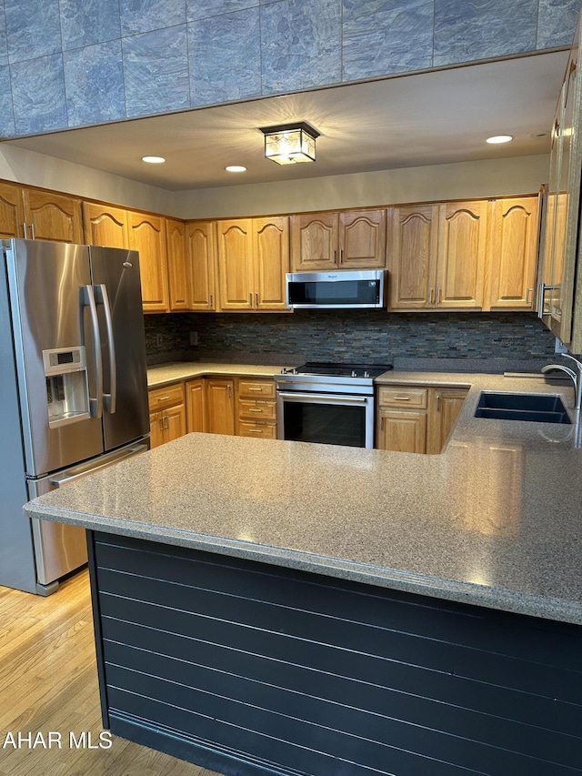 kitchen with tasteful backsplash, light wood-style flooring, appliances with stainless steel finishes, a peninsula, and a sink