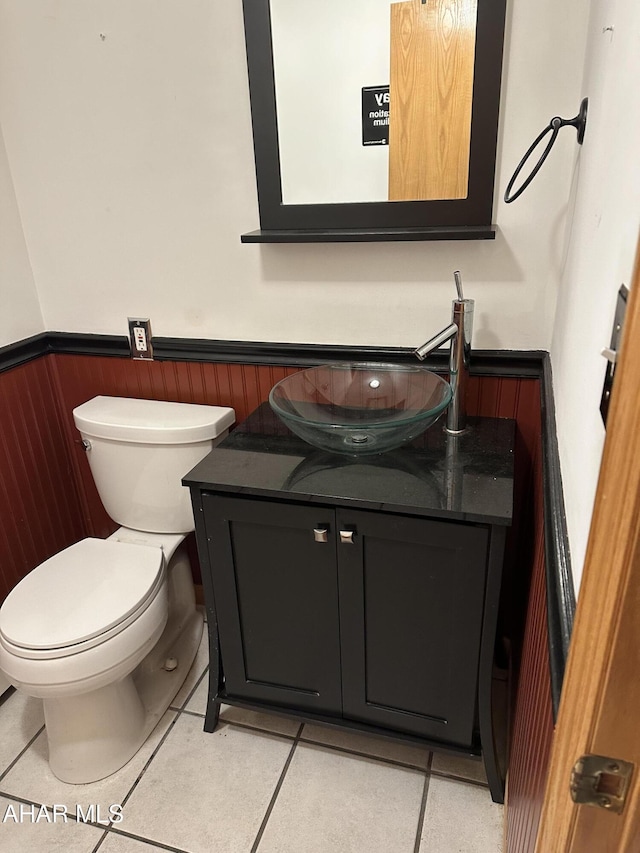 half bathroom featuring wooden walls, a wainscoted wall, toilet, tile patterned floors, and vanity