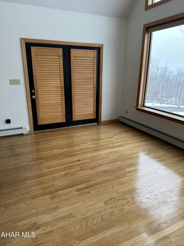 empty room featuring a baseboard heating unit, lofted ceiling, and light wood-style flooring