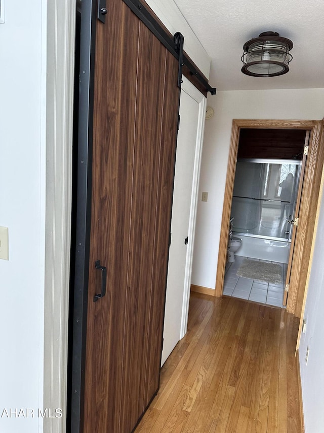 corridor with light wood finished floors, baseboards, and a barn door