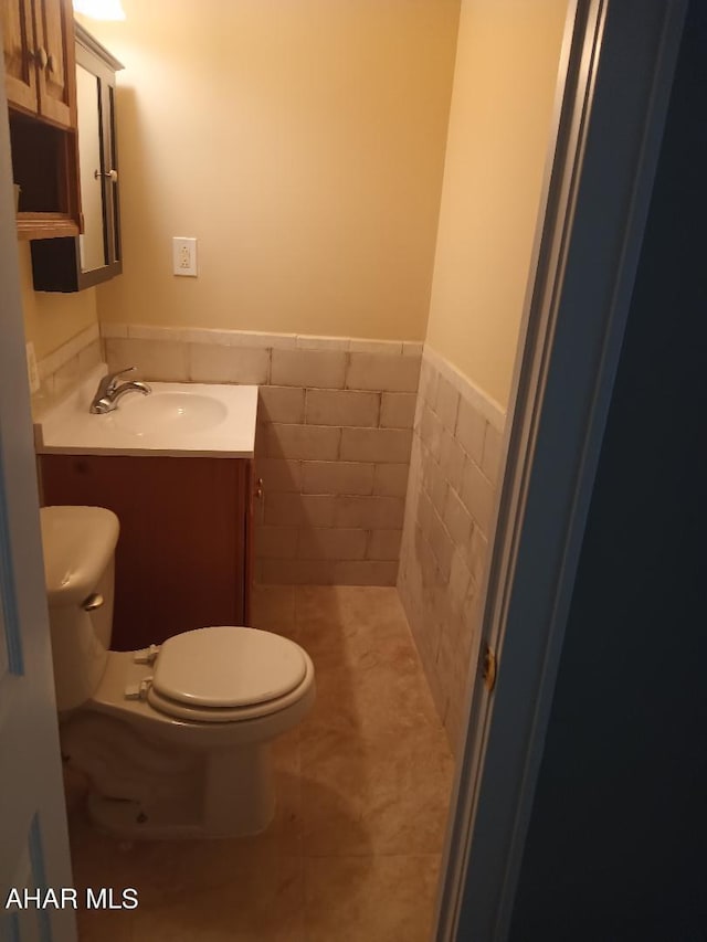 bathroom featuring tile patterned floors, vanity, toilet, and tile walls