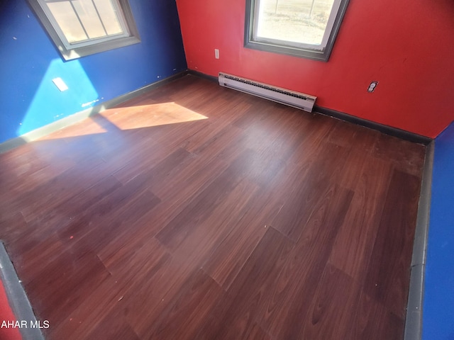 empty room featuring baseboards, a baseboard heating unit, and wood finished floors