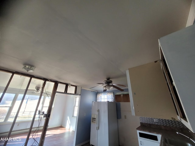 kitchen with dark countertops, a baseboard radiator, ceiling fan, white fridge with ice dispenser, and a sink