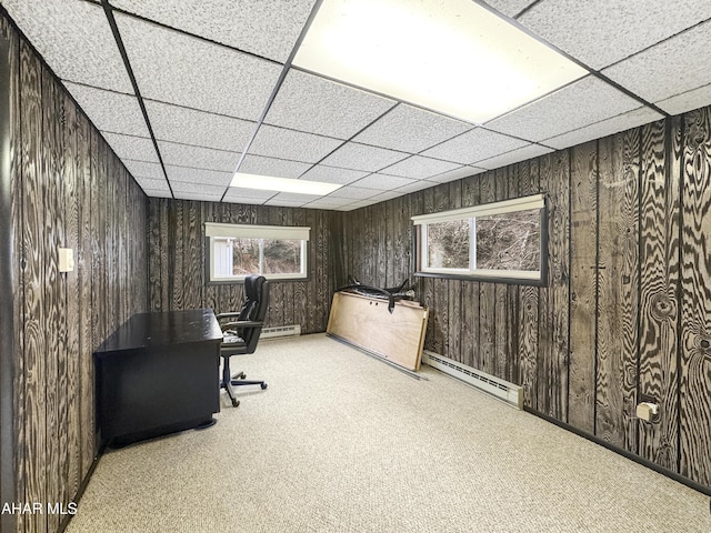 office area with a paneled ceiling, light carpet, wooden walls, and a baseboard heating unit