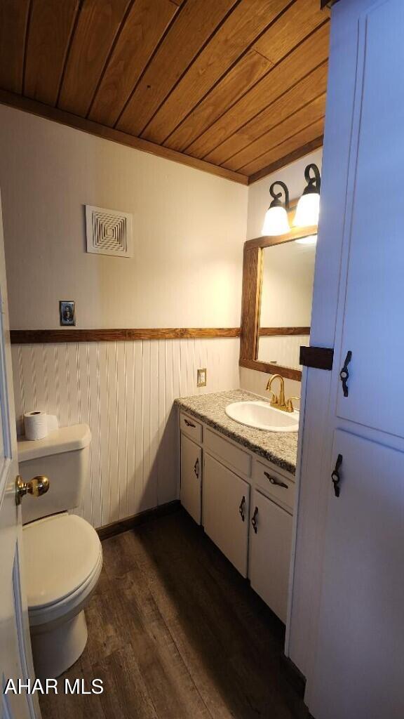 bathroom featuring wood walls, wood-type flooring, vanity, toilet, and wooden ceiling