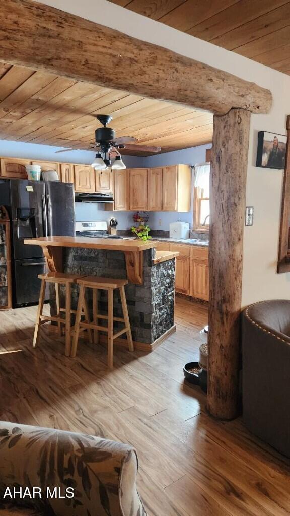 kitchen with a breakfast bar, light hardwood / wood-style flooring, wooden ceiling, refrigerator with ice dispenser, and beamed ceiling