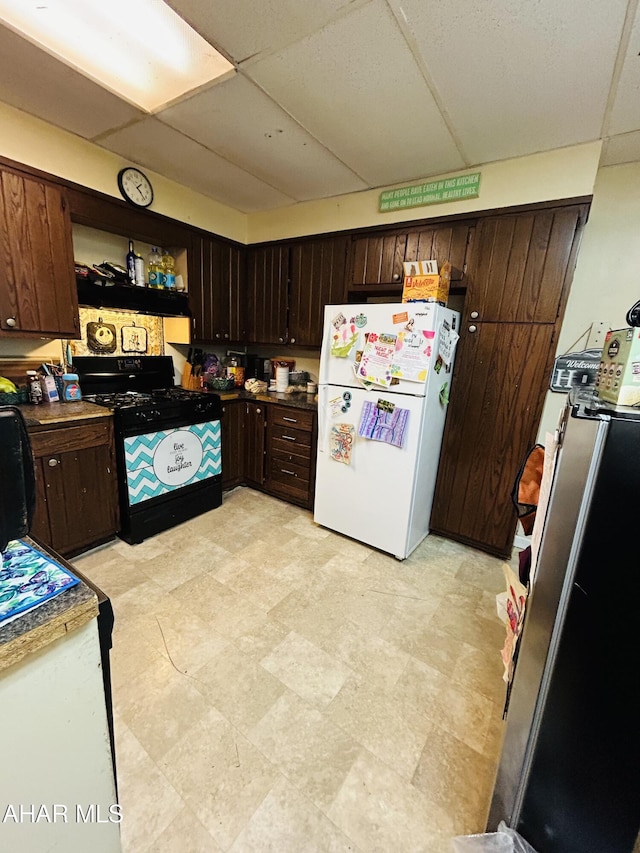 kitchen with freestanding refrigerator, black range with gas cooktop, a paneled ceiling, and dark brown cabinetry