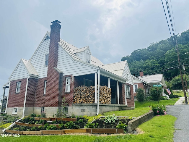 14 W 2nd St, Everett, PA 15537 - view of side of home featuring a vegetable garden, brick siding, a porch, a chimney, and a metal roof