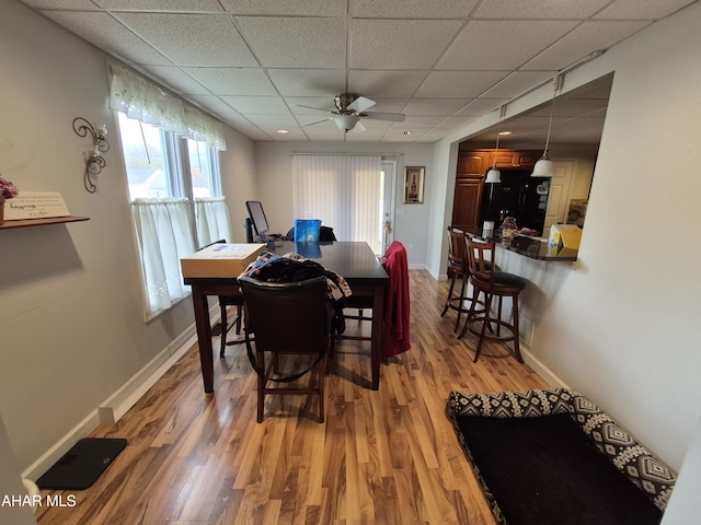 dining room featuring light wood-type flooring, a ceiling fan, baseboards, and a paneled ceiling