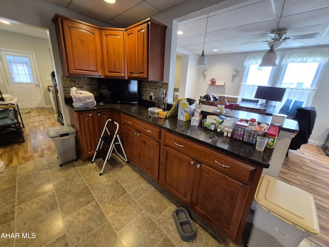 kitchen with dark stone countertops, a paneled ceiling, a peninsula, tasteful backsplash, and ceiling fan