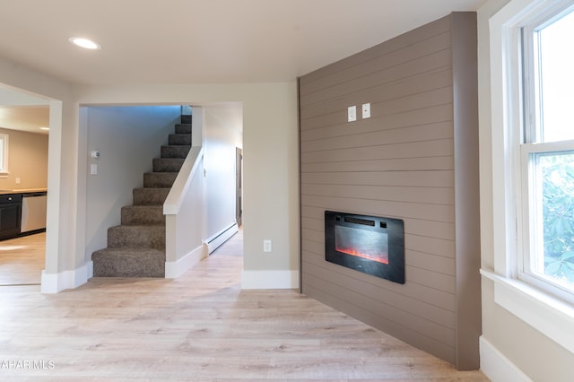 unfurnished living room with light hardwood / wood-style flooring, a baseboard heating unit, a wealth of natural light, and a large fireplace