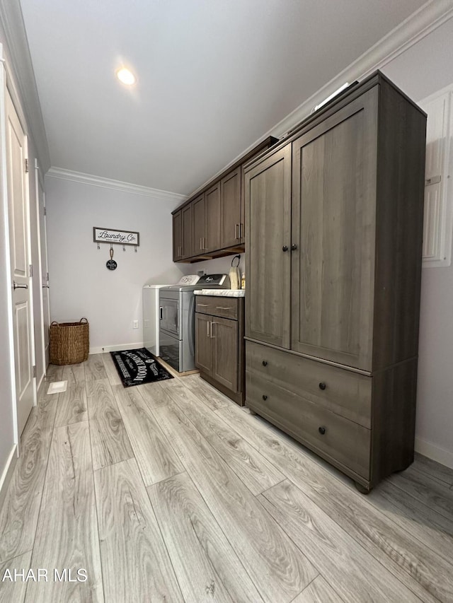 washroom featuring crown molding, cabinet space, baseboards, separate washer and dryer, and light wood-style flooring