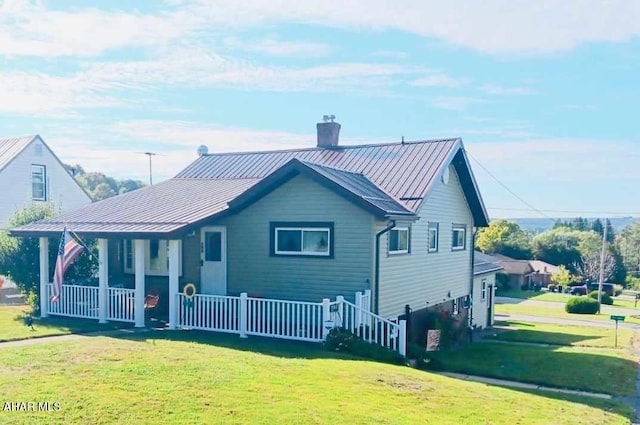 rear view of property with a lawn, a standing seam roof, covered porch, metal roof, and a chimney