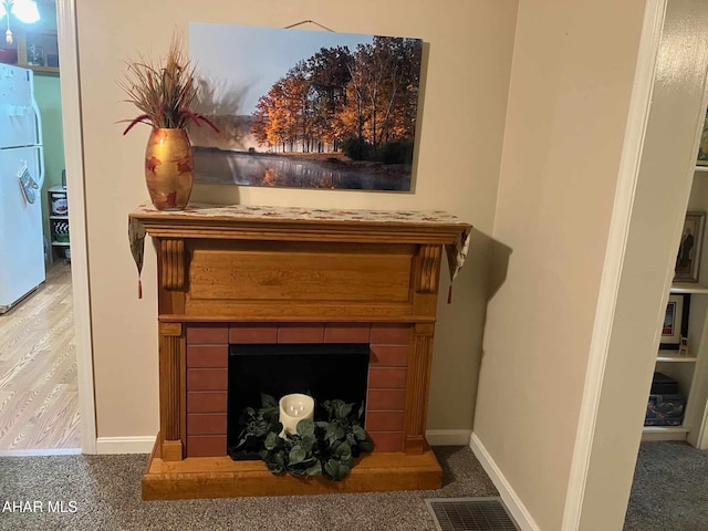 room details featuring a fireplace, visible vents, freestanding refrigerator, and baseboards