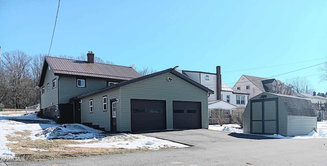 exterior space with a storage unit, an outbuilding, an attached garage, metal roof, and a chimney