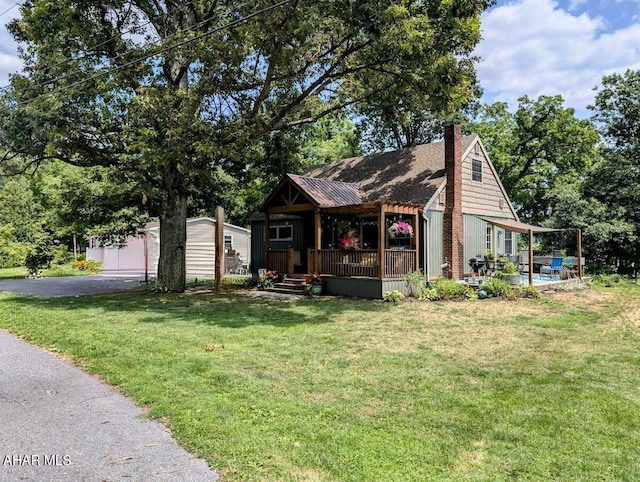 view of front of home with covered porch, a garage, a front lawn, and an outdoor structure