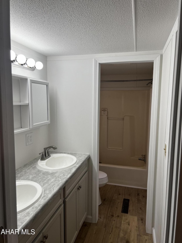 full bathroom with a textured ceiling, toilet, vanity, bathtub / shower combination, and hardwood / wood-style flooring