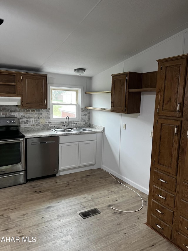 kitchen featuring sink, backsplash, vaulted ceiling, appliances with stainless steel finishes, and light wood-type flooring