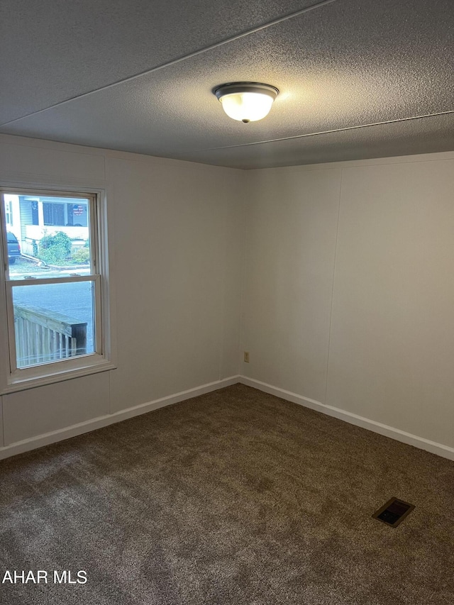 spare room with dark colored carpet and a textured ceiling