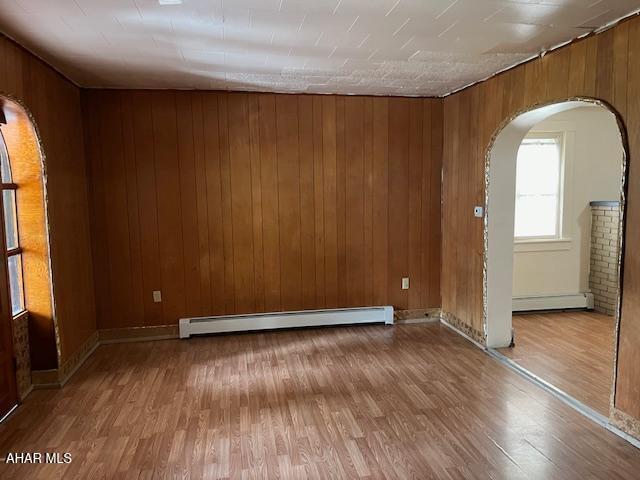 1008 21st Ave, Altoona, PA 16601 - empty room featuring a baseboard heating unit, arched walkways, a baseboard radiator, wood finished floors, and wood walls