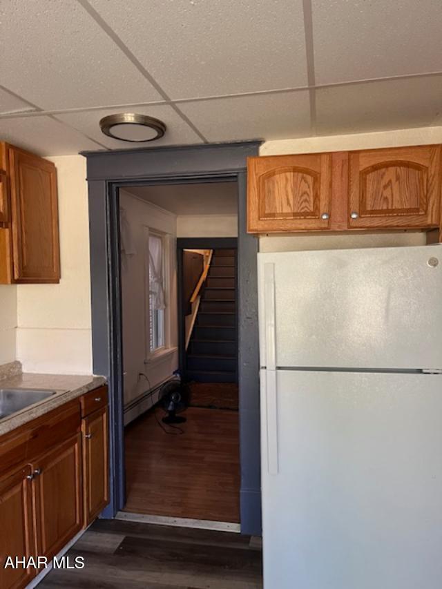 1008 21st Ave, Altoona, PA 16601 - kitchen with freestanding refrigerator, dark wood-style flooring, a drop ceiling, a baseboard radiator, and brown cabinetry