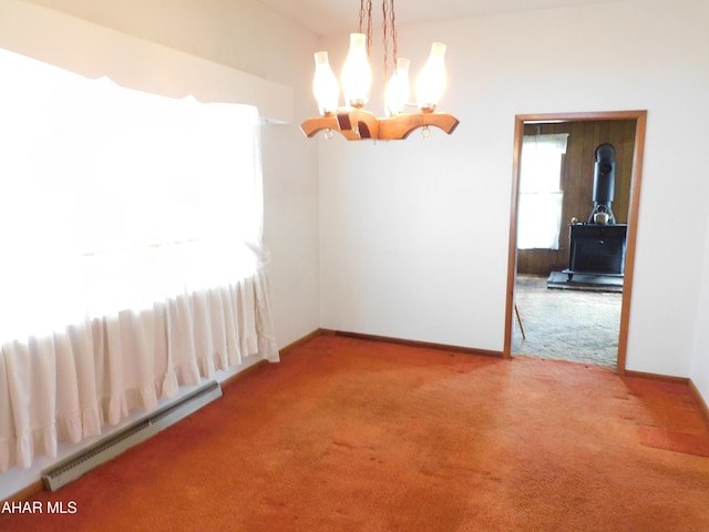 carpeted spare room featuring a baseboard radiator, a wood stove, a chandelier, and baseboards