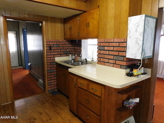 kitchen featuring a sink, brown cabinetry, light countertops, wood walls, and open shelves