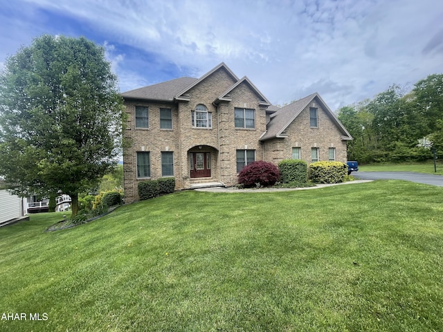 view of front facade featuring a front lawn, a shingled roof, and brick siding