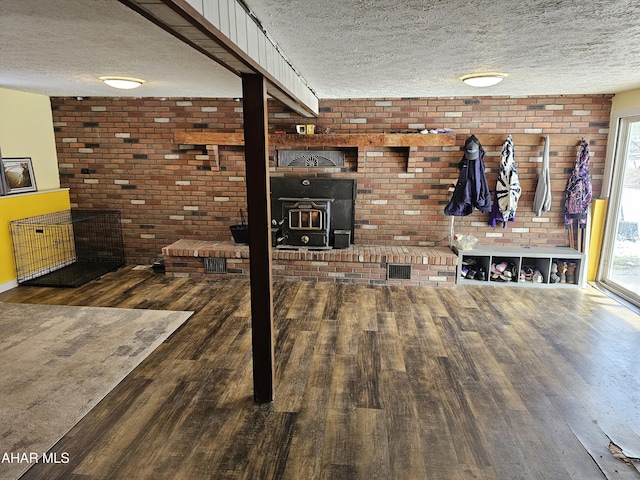 interior space with a textured ceiling, dark hardwood / wood-style flooring, a wood stove, and brick wall