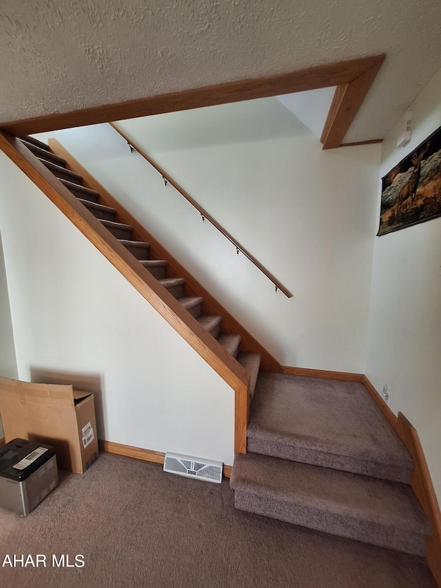 stairway with carpet flooring and a textured ceiling