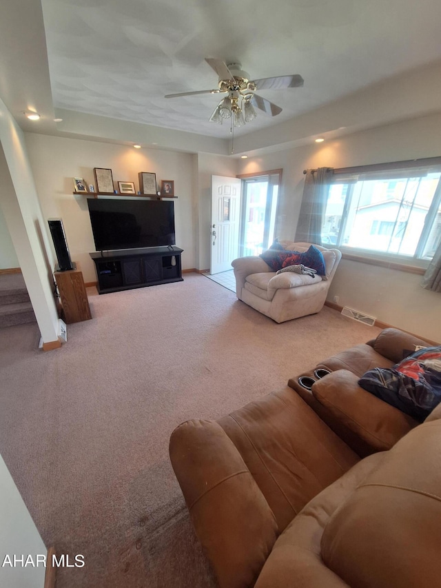 living room with a tray ceiling, ceiling fan, and carpet floors