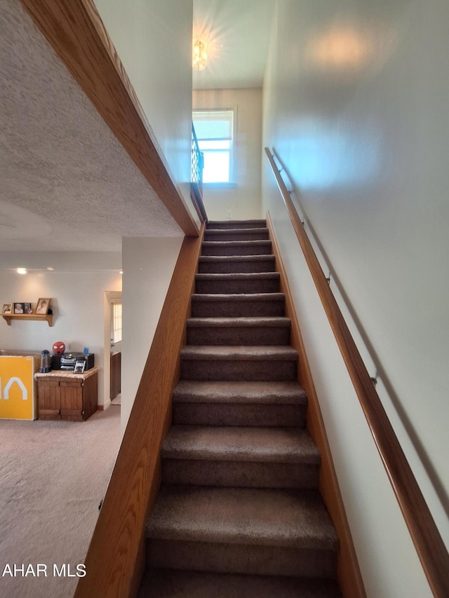 staircase featuring carpet floors and a textured ceiling