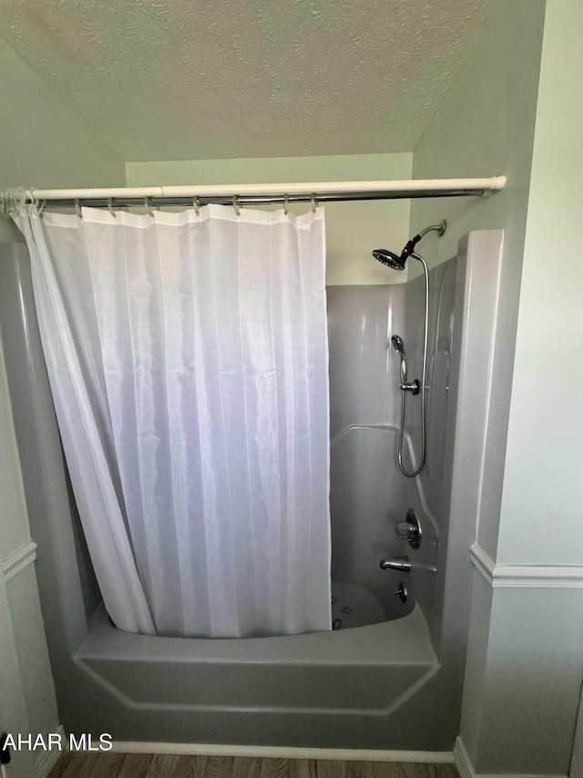 bathroom featuring hardwood / wood-style flooring, shower / bath combination with curtain, and a textured ceiling