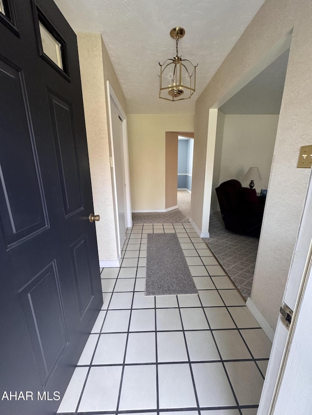 hall with light tile patterned floors, a textured ceiling, and an inviting chandelier