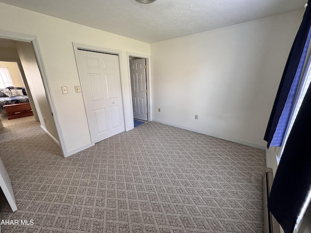 unfurnished bedroom featuring light carpet, a textured ceiling, and a baseboard heating unit