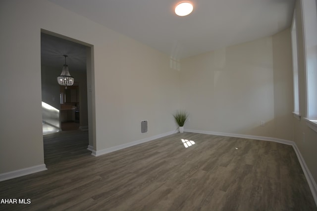 empty room with dark wood-type flooring and an inviting chandelier