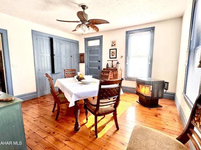 dining area featuring light wood-type flooring, a wood stove, a textured ceiling, and baseboards