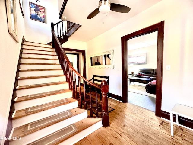 stairway featuring a ceiling fan, baseboards, and wood finished floors