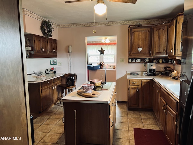 kitchen featuring dark brown cabinetry, ceiling fan, a center island, washing machine and dryer, and light tile patterned floors