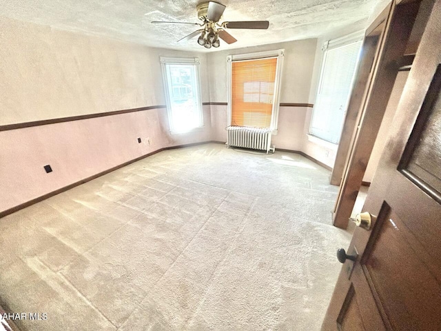 unfurnished room with a textured ceiling, light colored carpet, radiator, and ceiling fan