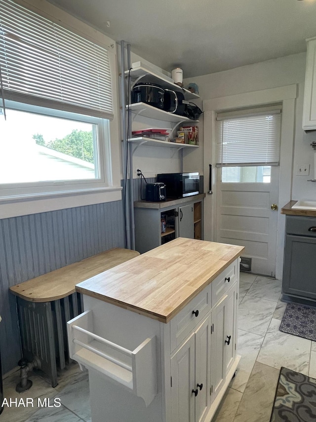 523 W 16th St, Tyrone, PA 16686 - kitchen featuring butcher block counters, light marble finish flooring, stainless steel microwave, white cabinets, and a wainscoted wall