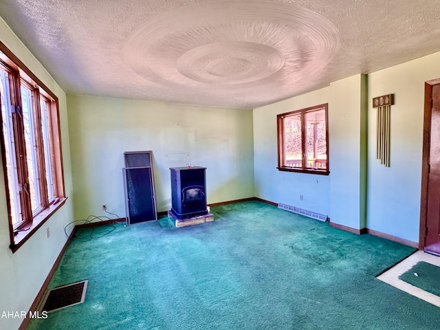 carpeted empty room with a wealth of natural light, visible vents, and a wood stove